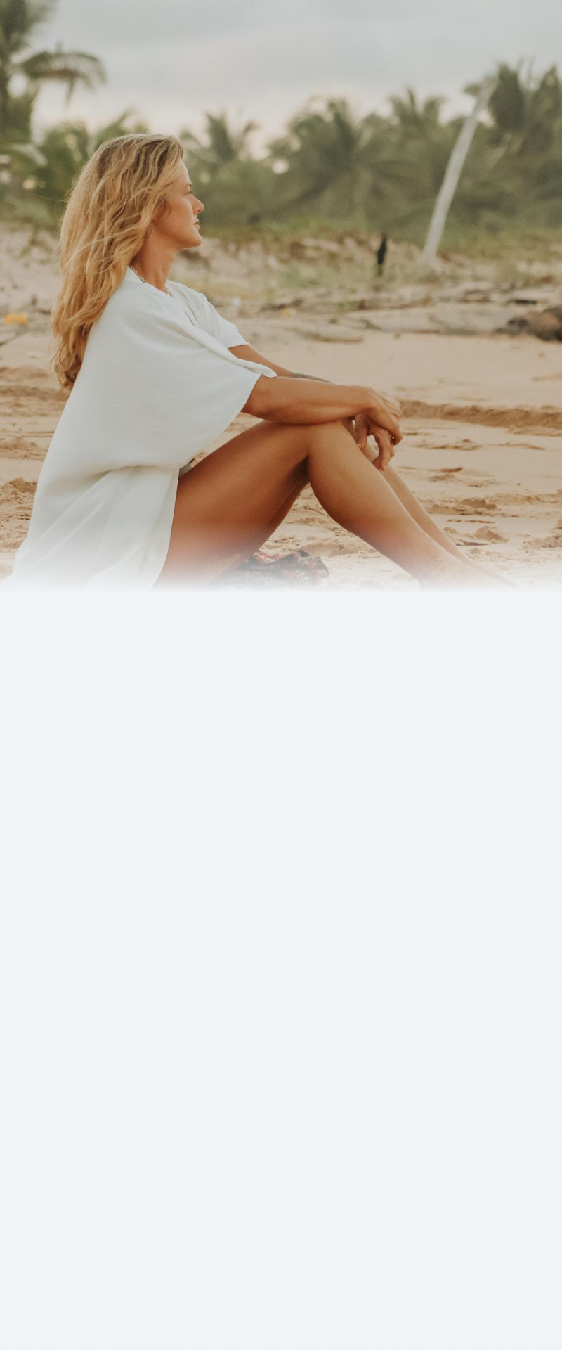 Juliana Spelta sentada na areia da praia, observando o horizonte.